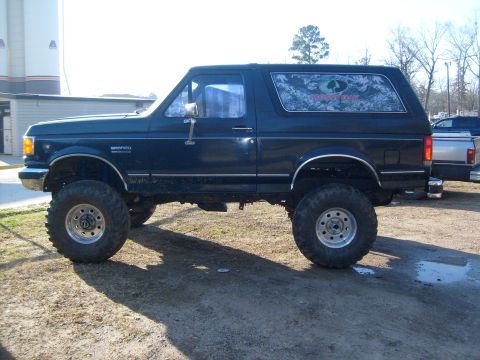 1989 Ford Bronco - A lifted 1989 Ford Bronco with custom window decals is parked outdoors on a sunny day.
