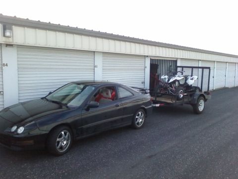 1995 Ford Bronco - A black coupe is seen from the side, towing a trailer loaded with ATVs in front of a row of storage units.