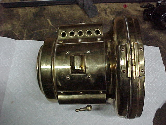 Polished brass headlamp housing on workbench showing vent holes, hinge and gas fitting