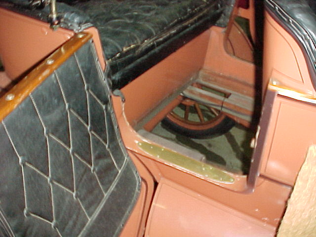 Antique car rear doorway: tufted black leather seat, brass sill plate, wood-spoke wheel