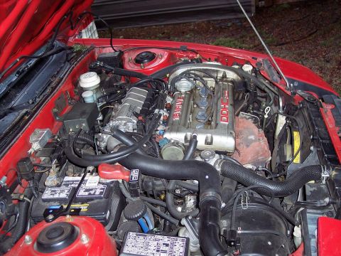 1991 Mitsubishi Eclipse - The engine bay of a red car is shown with the hood open, revealing the V6 DOHC engine and associated parts.