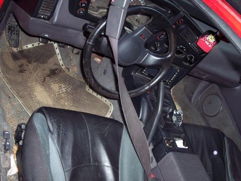1991 Mitsubishi Eclipse - The interior of a 1991 Mitsubishi Eclipse reveals worn black leather seats and a cluttered dashboard.