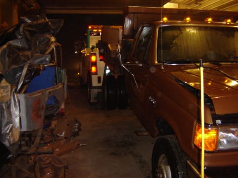 1992 Ford Bronco - A brown Ford F-Series truck and a tow truck are parked indoors. The Ford appears to be from the early 1990s.