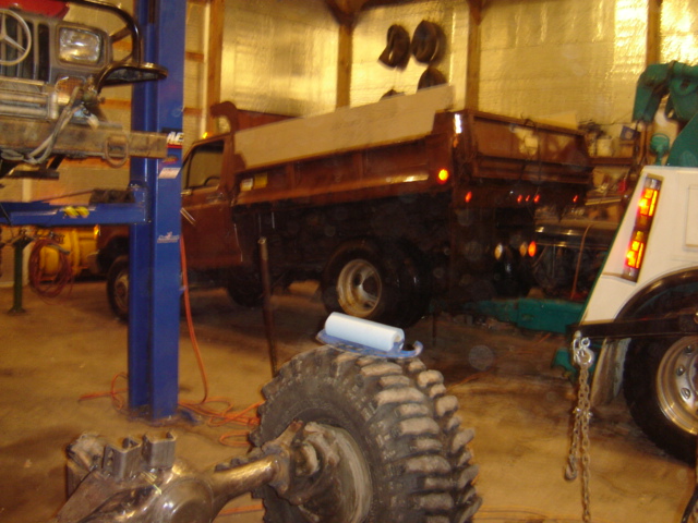 Dump truck with a wooden bed extension, seen from the rear quarter angle in a garage