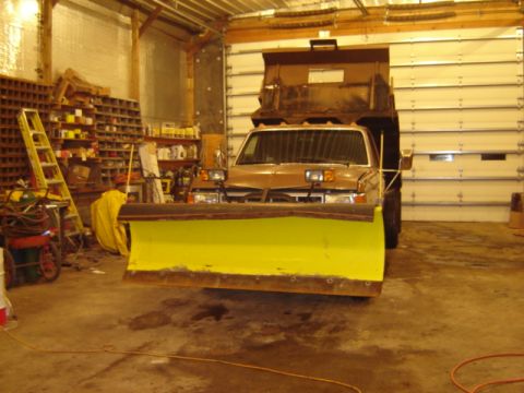 1992 Ford Bronco - A dump truck equipped with a snow plow is parked in a garage, ready for winter conditions.