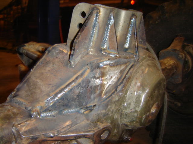 Close-up of a heavily welded metal component, possibly a differential housing or transfer case, with visible weld beads and mounting points