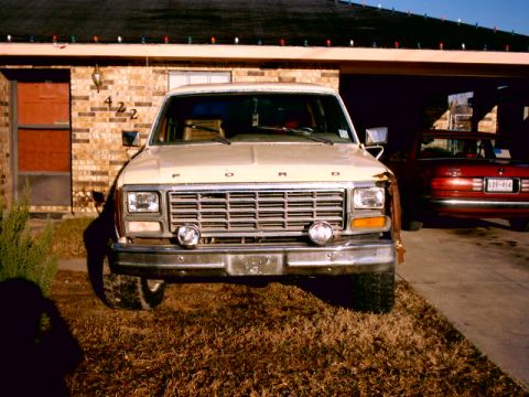 Tan early-80s Ford F-series pickup parked in front of a brick house at sunset