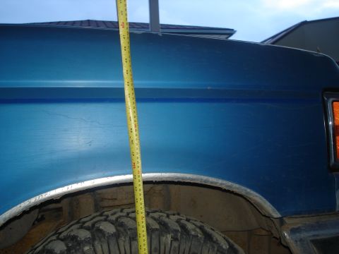 1990 Ford Bronco - A yellow measuring tape is placed against the side of a blue SUV, showing its height.