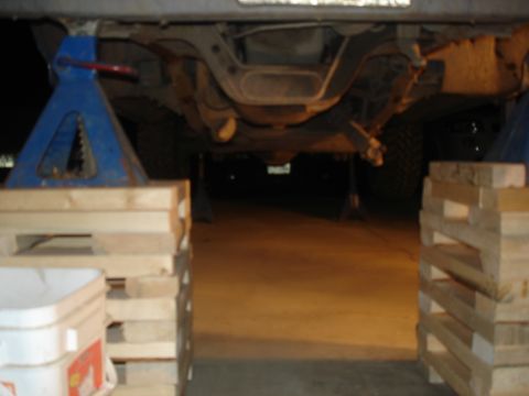 1990 Ford Bronco - The underside of a vehicle is supported by jack stands and wooden blocks, revealing its mechanical components.