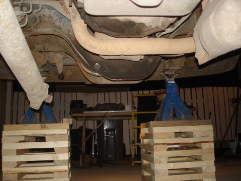 1990 Ford Bronco - The undercarriage of a vehicle is supported by jack stands and wooden blocks for maintenance.