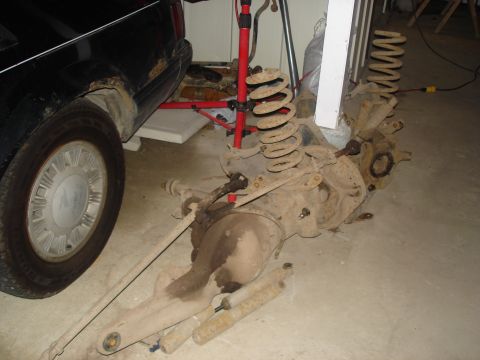 1990 Ford Bronco - Disassembled rear axle components are laid out on the floor next to a black vehicle with visible rust.
