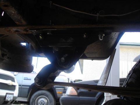 1990 Ford Bronco - Underside view of vehicle suspension components, with other vehicles partially visible in the background.