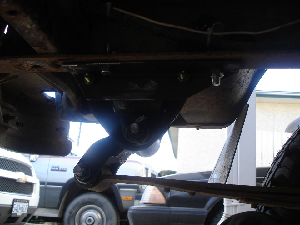 Underside of a vehicle with suspension components and a tire visible; other vehicles in background