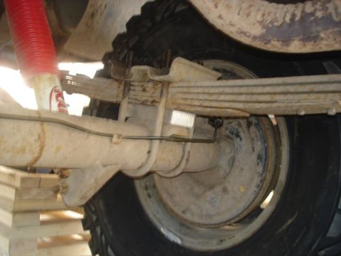 1990 Ford Bronco - Undercarriage view of a vehicle's rear axle, leaf springs, and a red shock absorber.