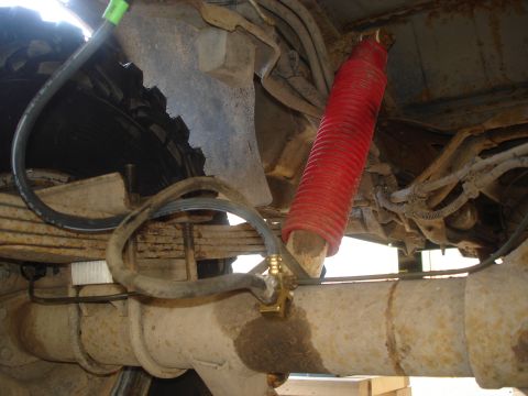 1990 Ford Bronco - Underside view of a vehicle's rear suspension system, showing a red shock absorber and leaf springs.