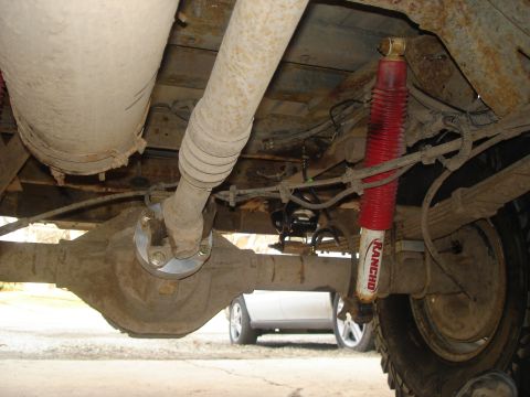 1990 Ford Bronco - Undercarriage components including differential, driveshaft, and shock absorber. A second vehicle is in the background.