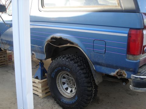 1990 Ford Bronco - The rear of a blue 1990 Ford Bronco shows significant rust damage around the wheel well and lower body panels.