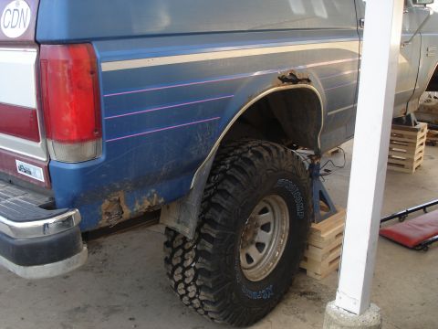 1990 Ford Bronco - Rear quarter panel and tire of a 1990 Ford Bronco, showing rust and off-road modifications.