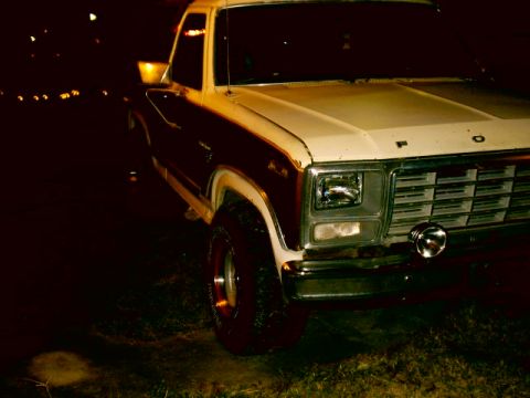 Front view of a white and maroon Ford F-Series truck at night. It has a chrome grille and a round fog light