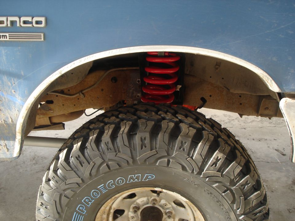 Blue Ford Bronco side view showing front tire, red coil spring, and fender well