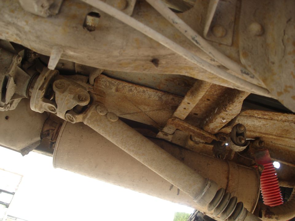 Underside view of a vehicle's driveshaft, exhaust pipe, and a red shock absorber