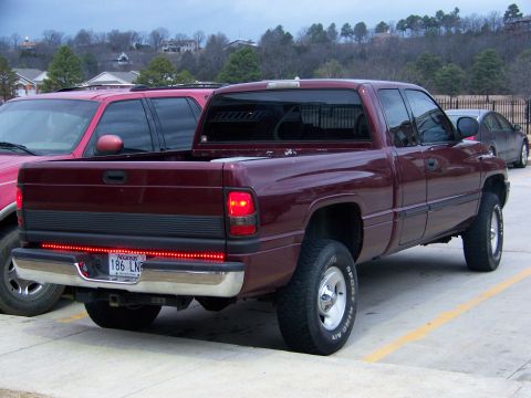 2001 Dodge 1500 - A maroon pickup truck is parked next to a red SUV, with a dark sedan in the background.