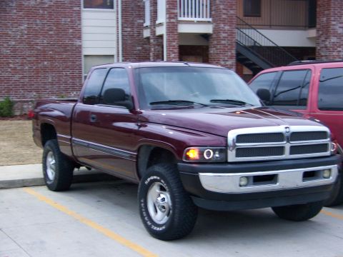 2001 Dodge 1500 - A maroon 2001 Dodge 1500 pickup truck is parked in front of a brick building, with another vehicle visible to its right.