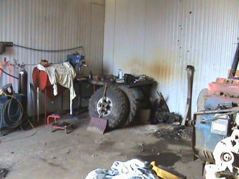 1967 Ford Bronco - Interior view of a cluttered garage workshop with various tools and large tires.