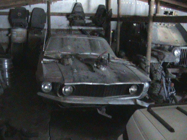 Dusty 1969 Ford Mustang with hood scoop and exposed engine parts, parked indoors