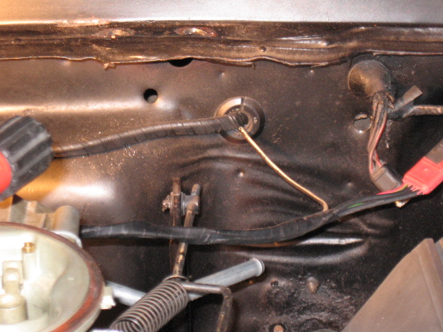 Close-up of engine bay showing wiring harness, firewall grommet, and part of a carburetor