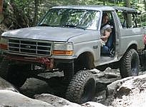 1986 Ford Bronco - Ford Bronco shown off-roading on a rocky trail. The grille suggests a 1990s model.