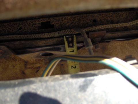 1978 Ford Bronco - A measuring tape is used to gauge a dimension on the rusty undercarriage of a vehicle.
