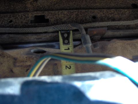 1978 Ford Bronco - A tape measure is used to gauge a distance on the underside of a vehicle, near some wiring.