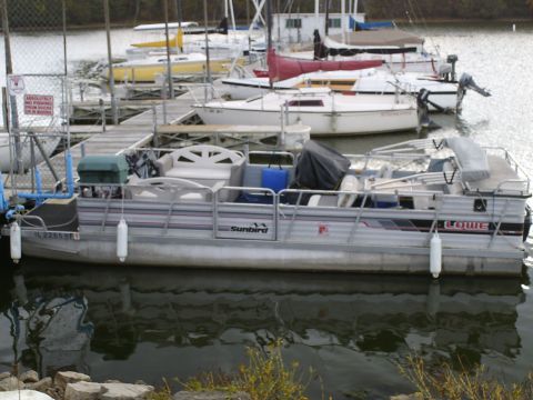 1983 Ford Bronco - A pontoon boat is docked at a marina alongside other watercraft.