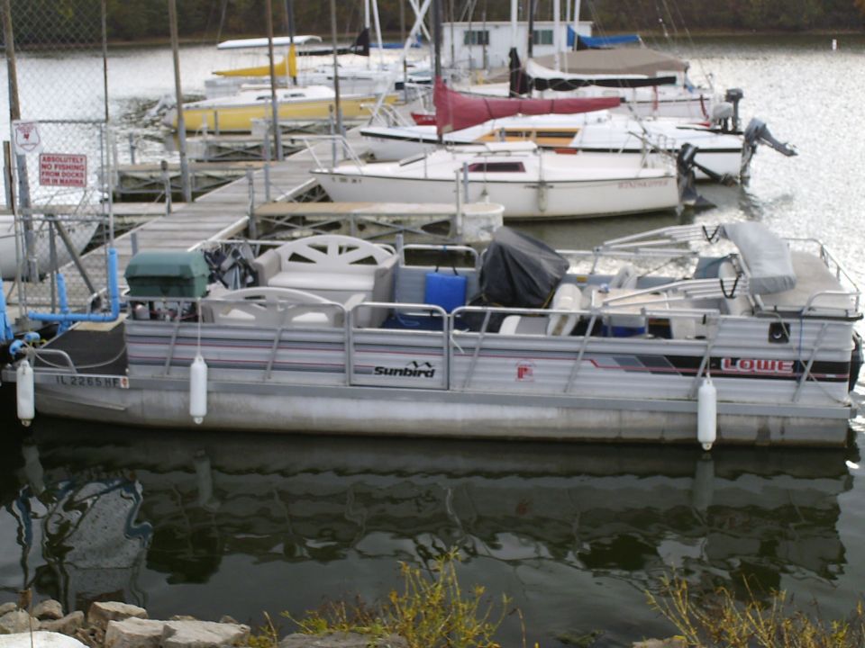Pontoon boat docked at a marina with other boats in the background. License plate reads IL 2265 HE