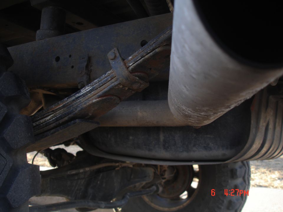 Underside view of a vehicle's suspension and exhaust system, showing leaf springs and a fuel tank
