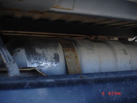 1979 Ford Bronco - Close-up of a vehicle's fuel tank, showing a rusty metal strap holding it in place.