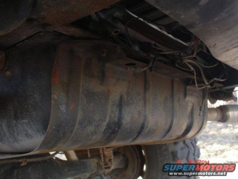 1978 Ford Bronco - The underside of a vehicle reveals a large, ribbed fuel tank with associated plumbing and electrical connections.