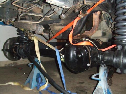 1996 Ford Bronco - Undercarriage of a vehicle undergoing repairs, showing suspension components and straps securing parts.