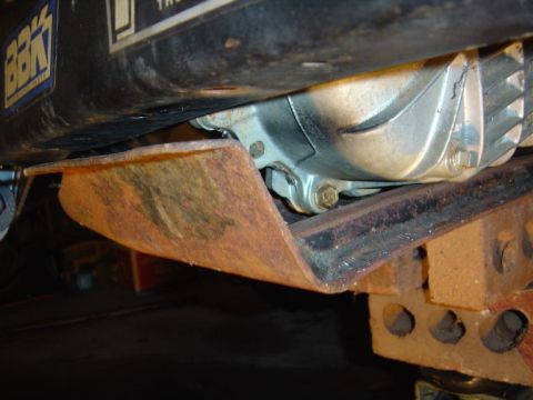 1986 Ford Bronco - Close-up view of a rusty skid plate and a component of the vehicle's drivetrain.