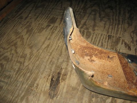 1994 Ford Bronco - A heavily rusted bumper part, likely from an older vehicle, is shown close-up on a wooden floor.