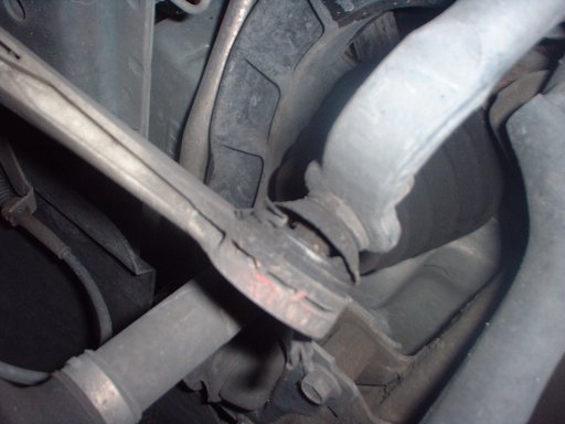 Underneath view of front suspension showing control arm, ball joint, and sway bar with rust and grime