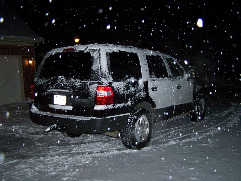 Rear view of a black 2004 Ford Expedition covered in snow at night