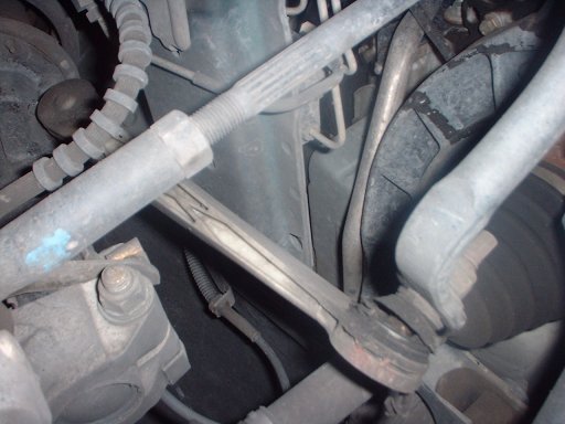 Underside view of front suspension: threaded tie rod, tie rod end, sway bar, and brake rotor with grime
