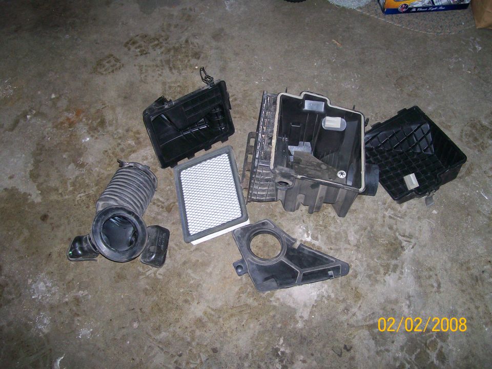 Disassembled black airbox, intake duct, and white air filter on concrete floor