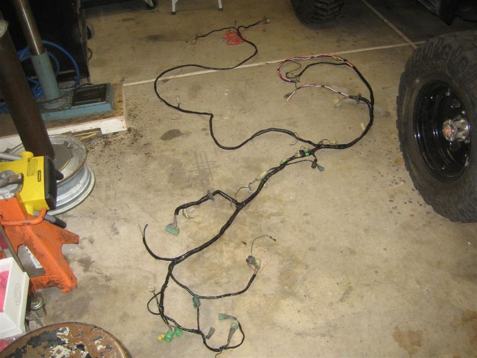 Vehicle wiring harness laid out on concrete floor next to a tire