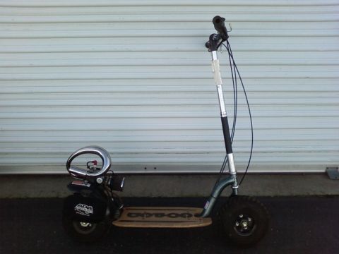 1995 Ford Bronco - A motorized scooter with a wooden deck and knobby tires is parked in front of a garage door.