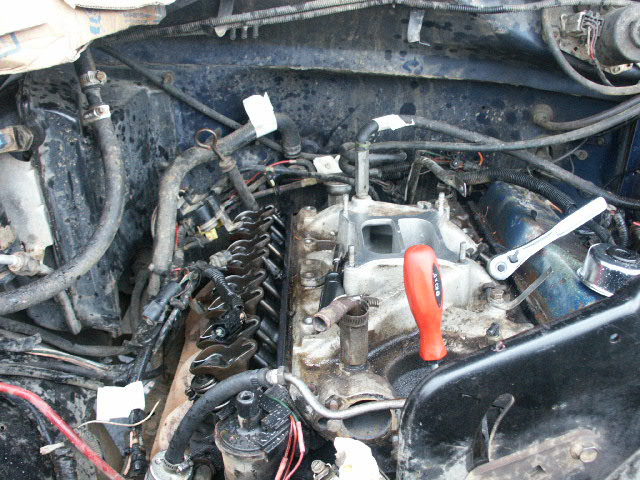 engine bay with valve covers removed, showing internal engine parts and a wrench