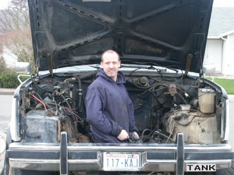 1984 Ford Bronco - A man poses in front of a truck's engine bay, which appears to be undergoing maintenance or a swap.