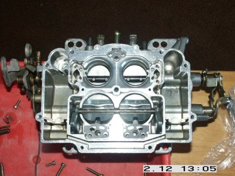 1984 Ford Bronco - Close-up of a disassembled carburetor, showing internal components and linkage mechanisms.
